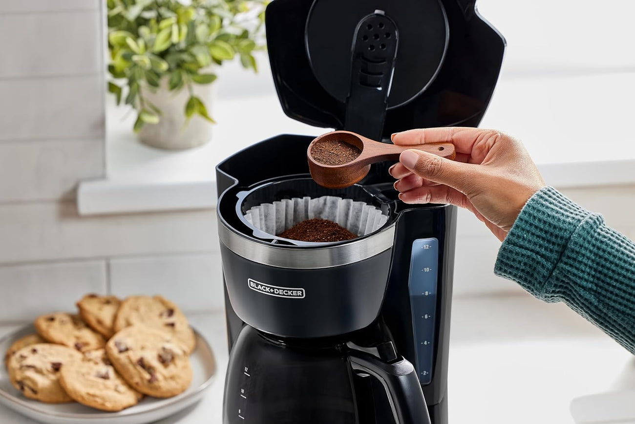 Ground coffee being added to a BLACK+DECKER coffee maker in a bright kitchen